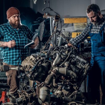 Dwóch mechaników pracuje nad naprawą silników w warsztacie samochodowym.