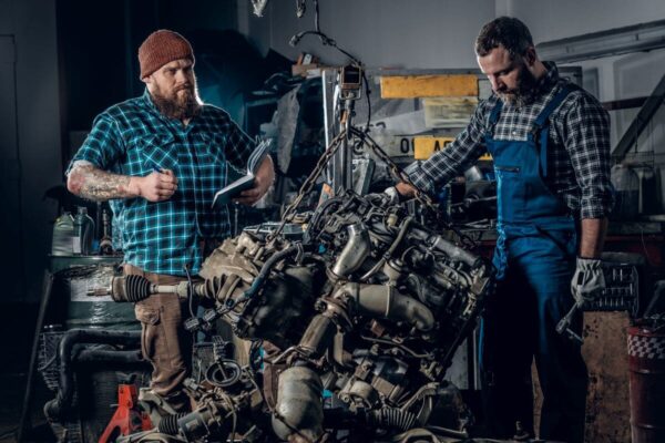 Dwóch mechaników pracuje nad naprawą silników w warsztacie samochodowym.