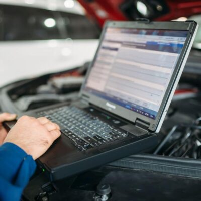 Mechanik wykonuje diagnostykę komputerową silników przy użyciu laptopa w warsztacie samochodowym.