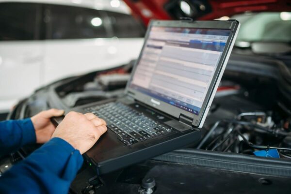 Mechanik wykonuje diagnostykę komputerową silników przy użyciu laptopa w warsztacie samochodowym.