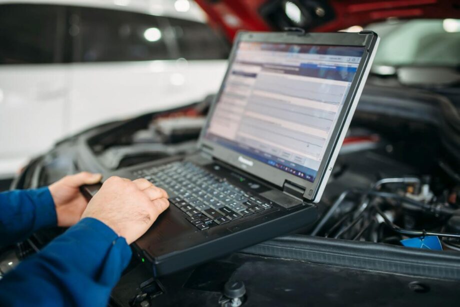 Mechanik wykonuje diagnostykę komputerową silników przy użyciu laptopa w warsztacie samochodowym.