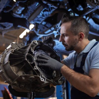 Mechanik skupiony na zadaniu wykonuje naprawę skrzyni biegów w warsztacie.