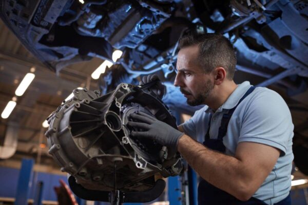 Mechanik skupiony na zadaniu wykonuje naprawę skrzyni biegów w warsztacie.