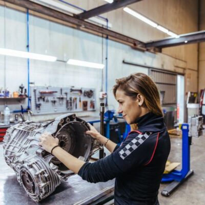 Kobieta pracuje w warsztacie nad naprawą skrzyni biegów.