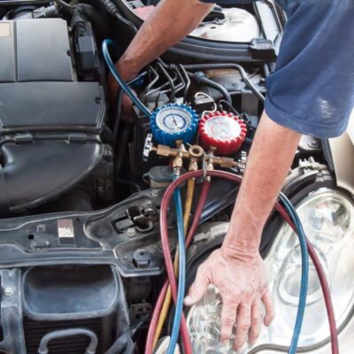 Mechanik zajmuje się naprawą klimatyzacji samochodowych, wykorzystując specjalistyczne narzędzia przy silniku auta.