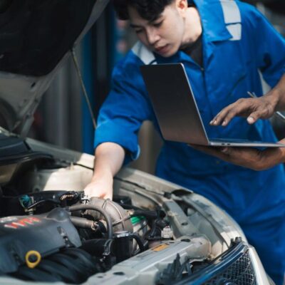 Mechanicy w warsztacie wykonują diagnostykę komputerową silnika za pomocą laptopa.