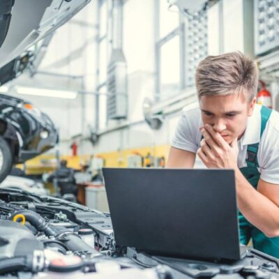 Mechanik wykonuje diagnostykę komputerową silnika w warsztacie samochodowym.