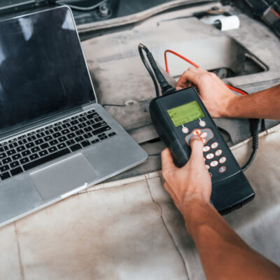 Osoba przeprowadza diagnostykę silników za pomocą komputera i elektronicznego urządzenia pomiarowego.