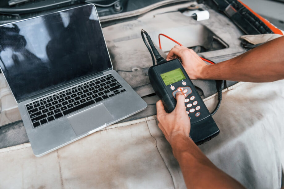 Osoba przeprowadza diagnostykę silników za pomocą komputera i elektronicznego urządzenia pomiarowego.