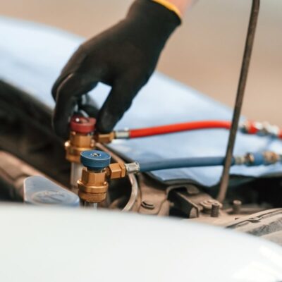 Ręka w rękawiczce obsługuje zawory podczas naprawy klimatyzacji w samochodzie.