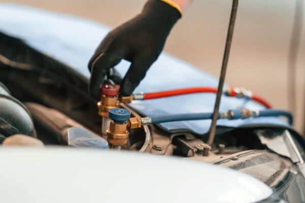 Ręka w rękawiczce obsługuje zawory podczas naprawy klimatyzacji w samochodzie.