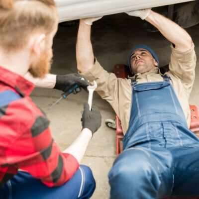 Dwóch mechaników pracuje pod pojazdem, koncentrując się na naprawie silników.