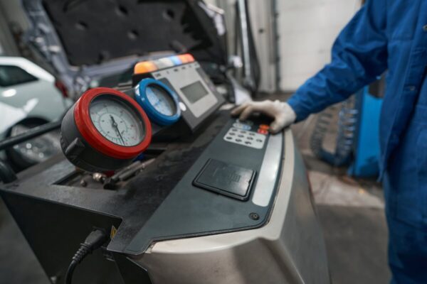 Technik w warsztacie wykonuje naprawę klimatyzacji samochodowych przy użyciu specjalistycznego sprzętu.