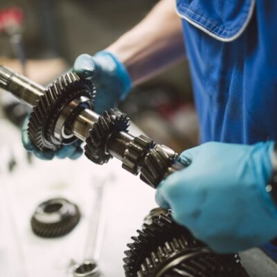 Mechanik w rękawiczkach pracuje nad naprawą skrzyni biegów.